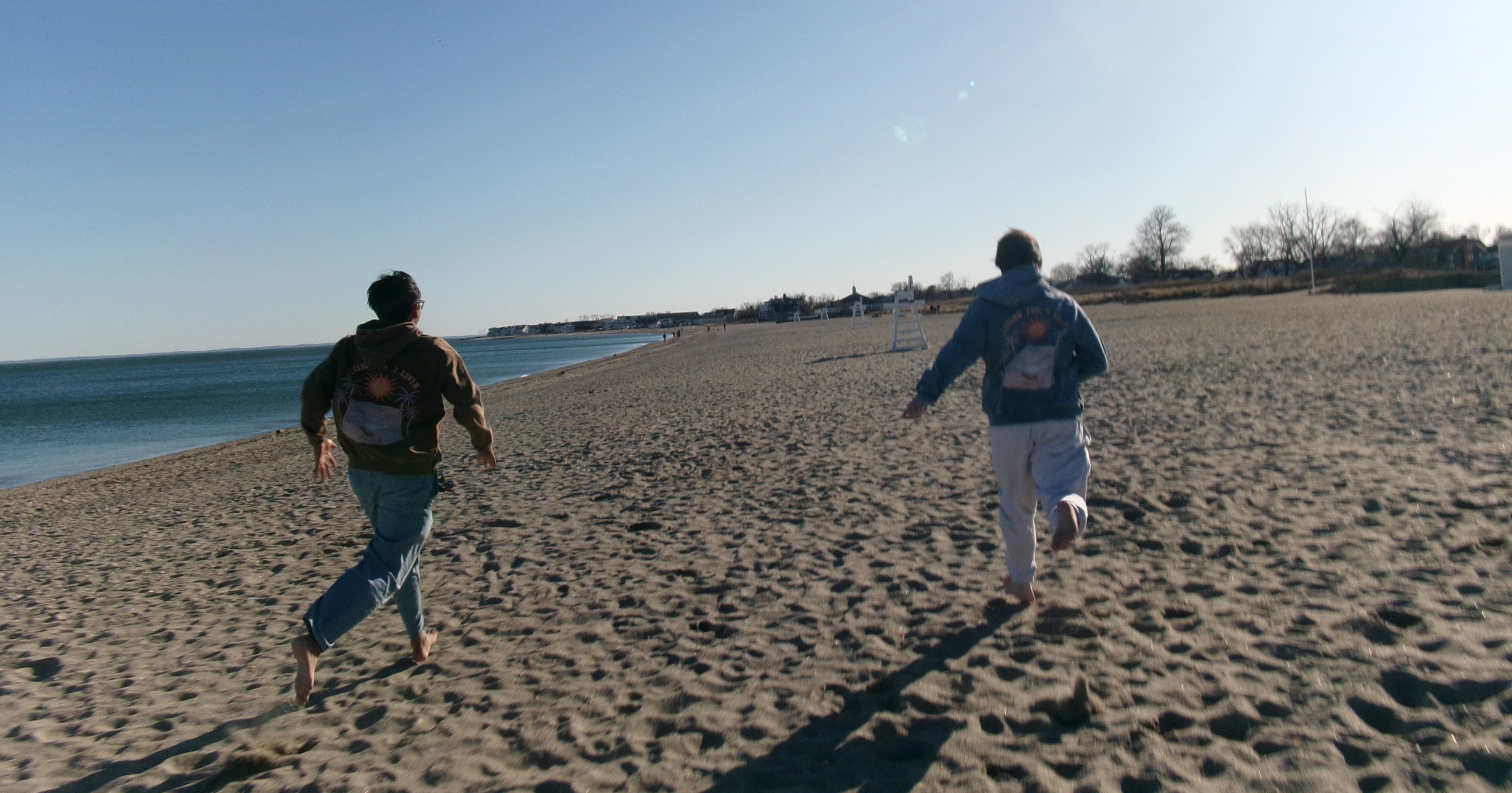 Two people running on a sandy beach with clear blue sky